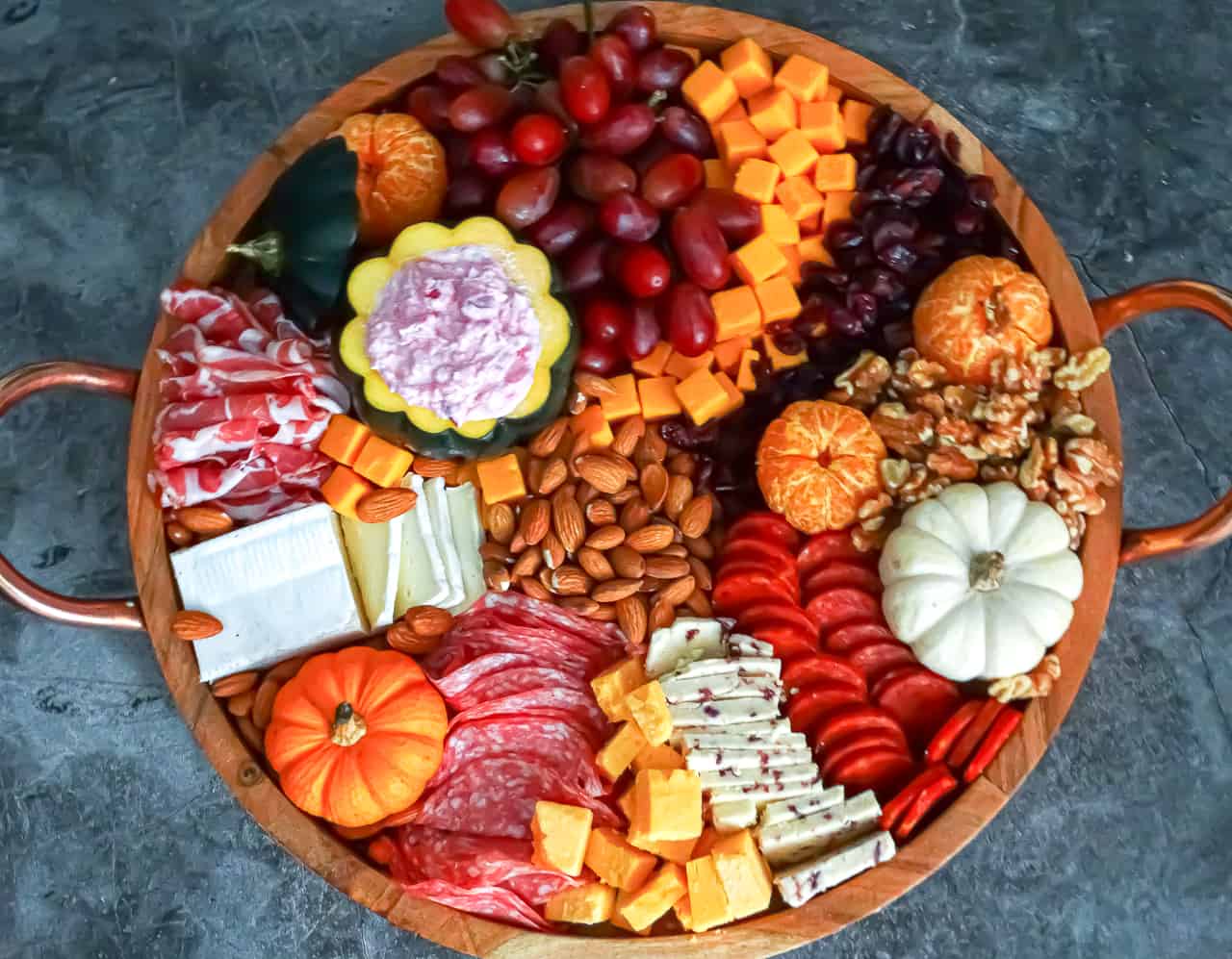 Thanksgiving charcuterie board filled with nuts, meats, cheeses, pumpkins and fruits in vibrat fall colors