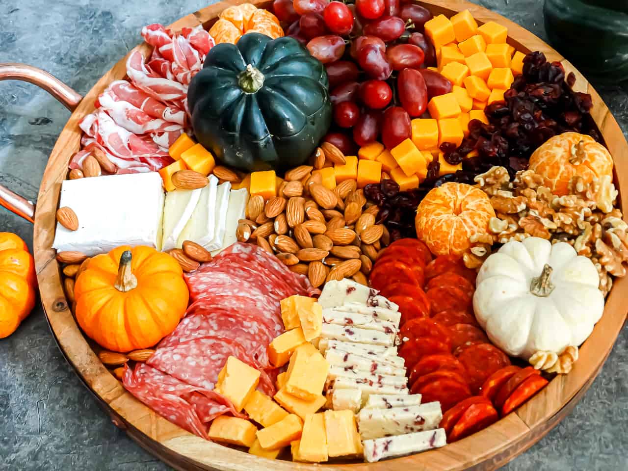 A Thanksgiving charcuterie board filled with nuts, cheese, pumpkins, and grapes