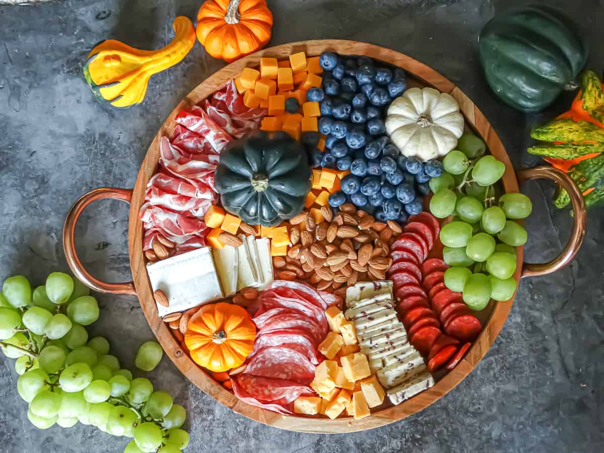 Meats, cheeses, fruits, nuts, and spreads arranged on a circular board intended to be an easy Thanksgiving appetizer