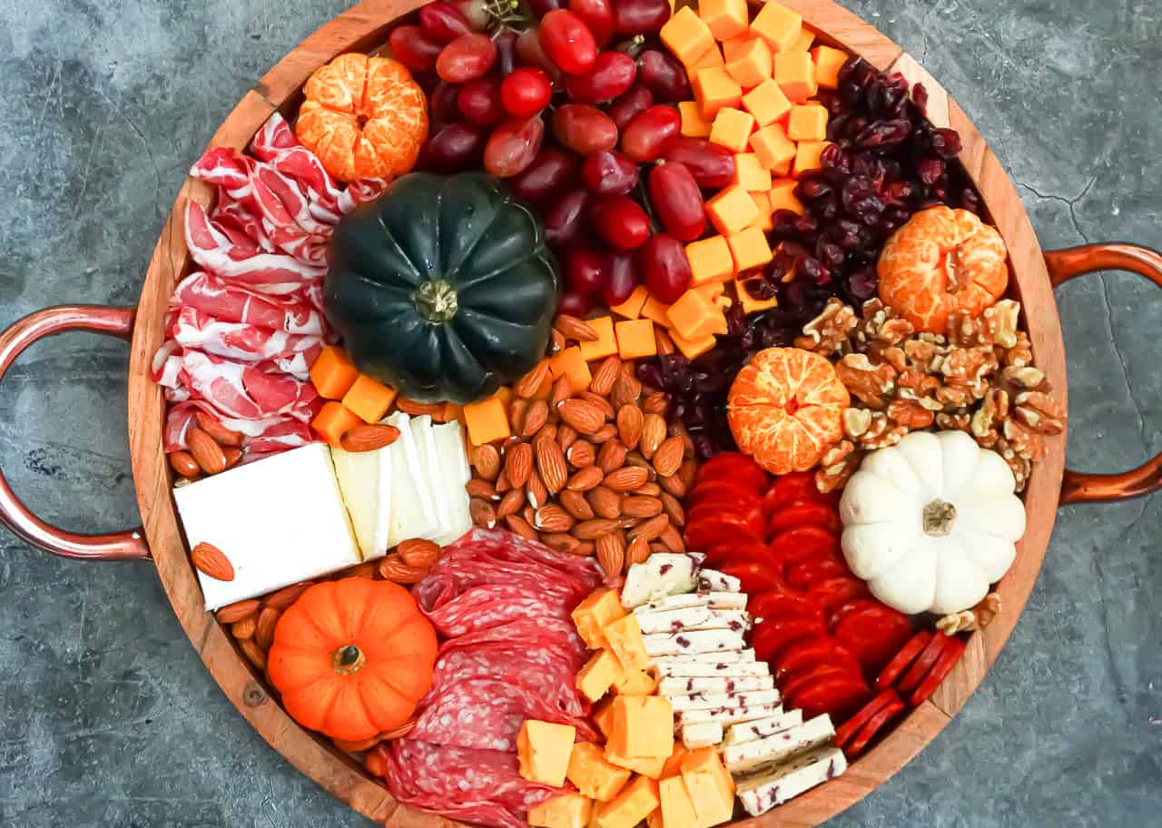 Meats, cheeses, fruits, nuts, and spreads arranged on a circular board intended to be an easy Thanksgiving appetizer
