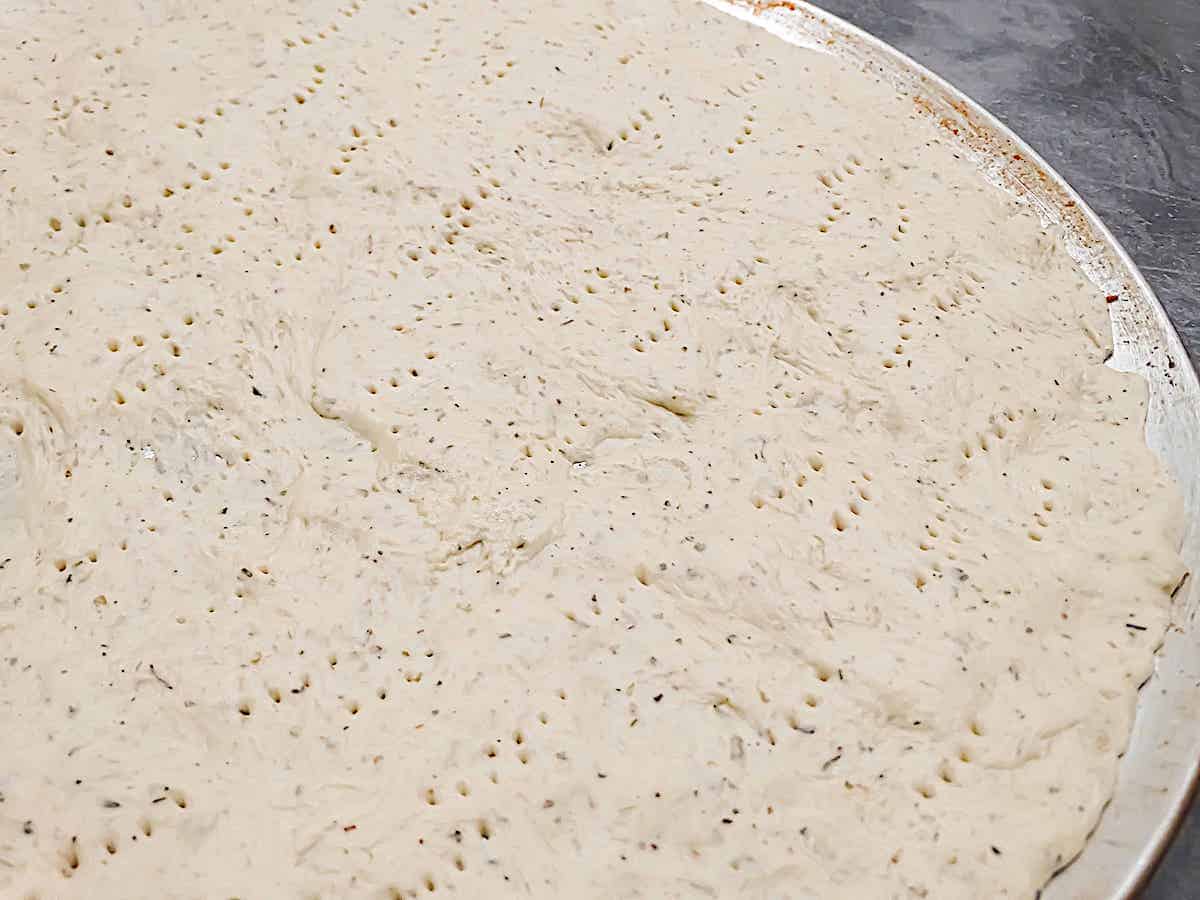 thin crust pizza dough spread on a pan with holes poked in the crust