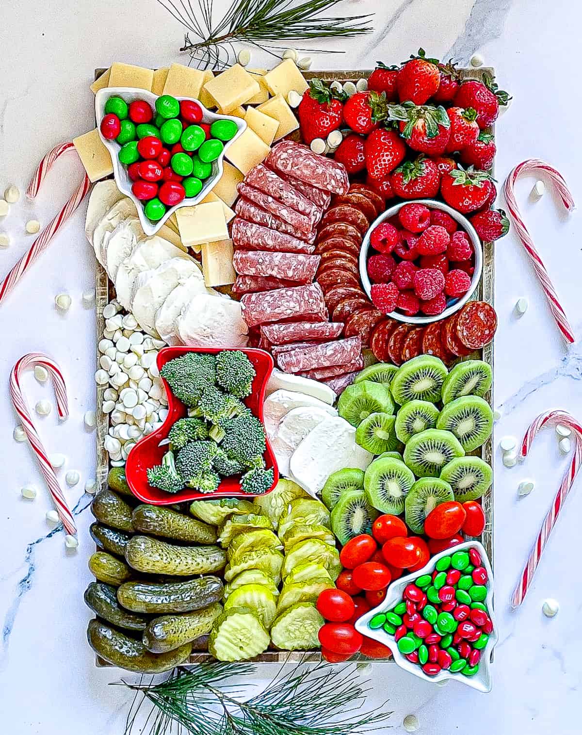 Christmas charcuterie board with red, white, and green fruits, vegetables, meats and cheeses surrounded by candy canes