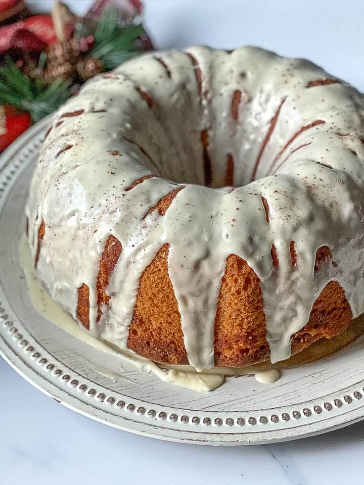 eggnog cake topped with eggnog glaze and nutmeg, on a white plate with Christmas flowers in the background