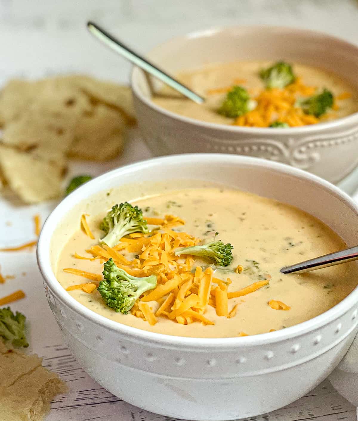 2 bowls of creamy instant pot broccoli cheddar soup, topped with extra broccoli and cheese