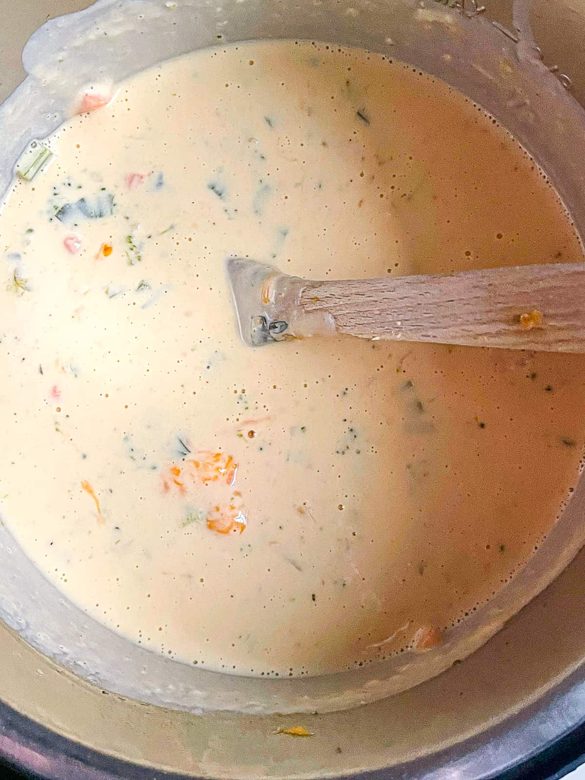 broccoli cheddar soup in the Instant pot, being mixed with cheddar cheese