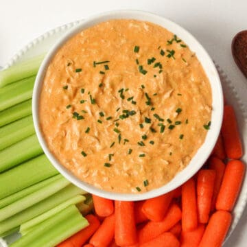 Instant Pot buffalo chicken dip topped with scallions in a white bowl surrounded by celery, carrots, and crackers