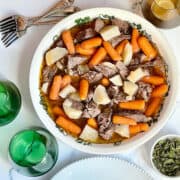 Instant Pot lamb stew in a white serving dish surrounded by utensils and plates
