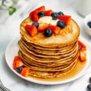 oat milk pancakes topped with syrup, strawberries and blueberries in a stack on a white plate