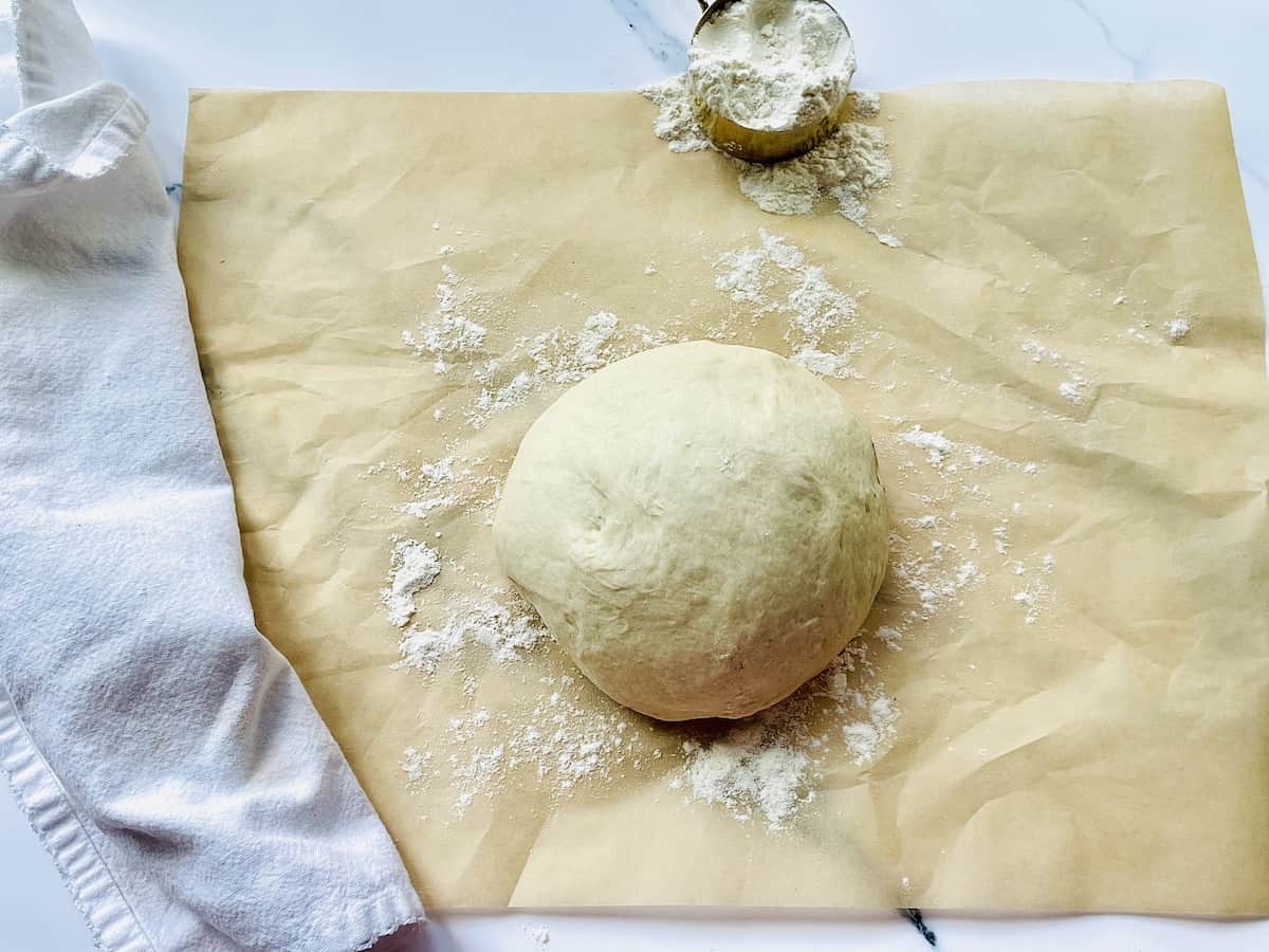 pizza dough ball rising on parchment paper