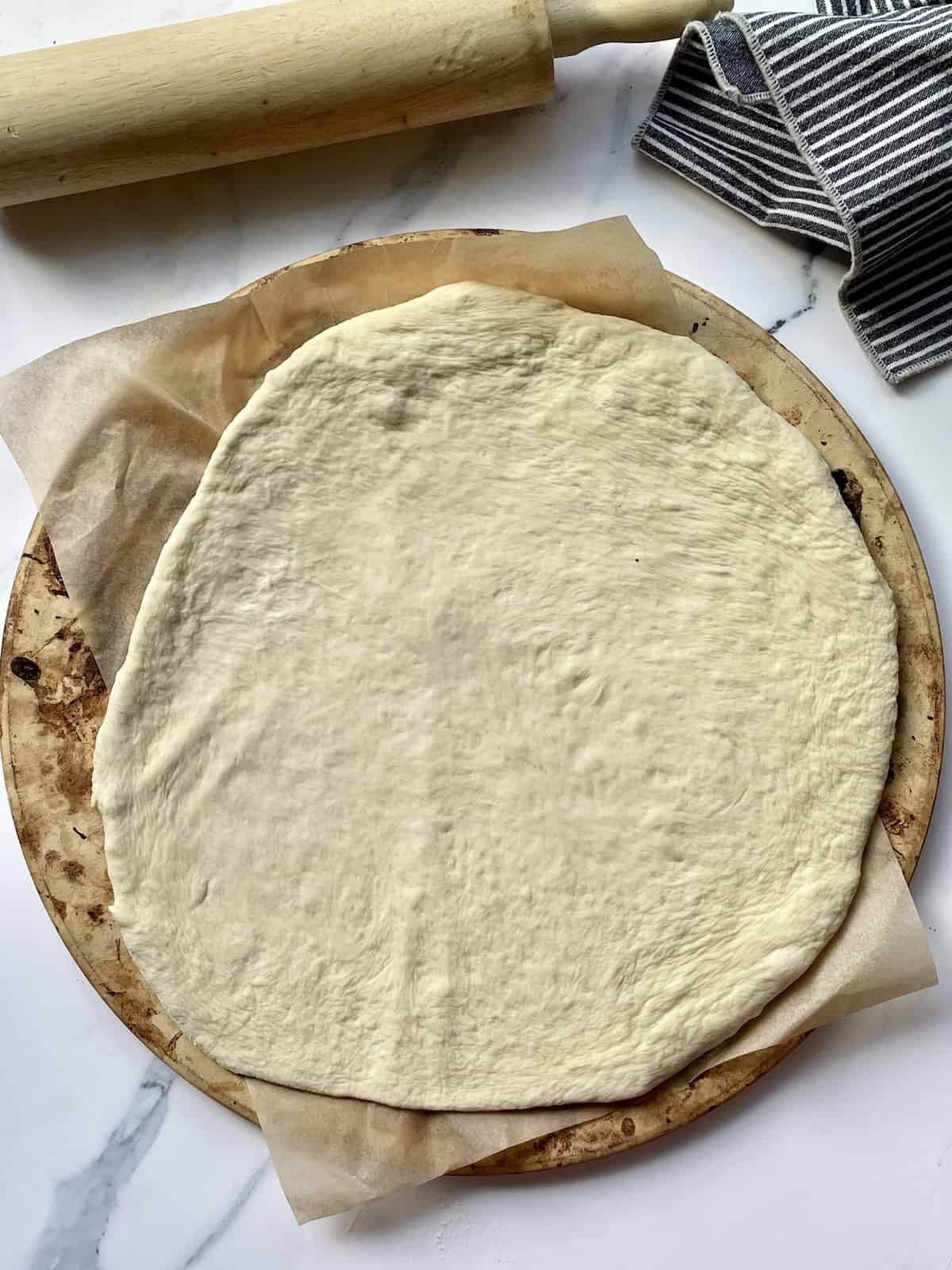 homemade pizza dough spread on a parchment paper and pizza stone