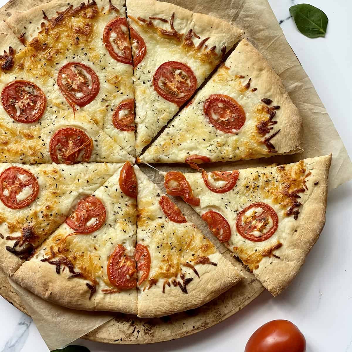 white pizza topped with tomatoes sliced on parchment paper