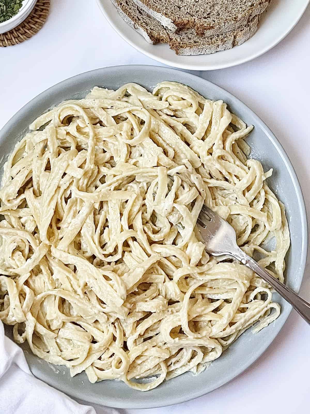 fettuccine alfredo in a bowl with cheese, bread, and herbs