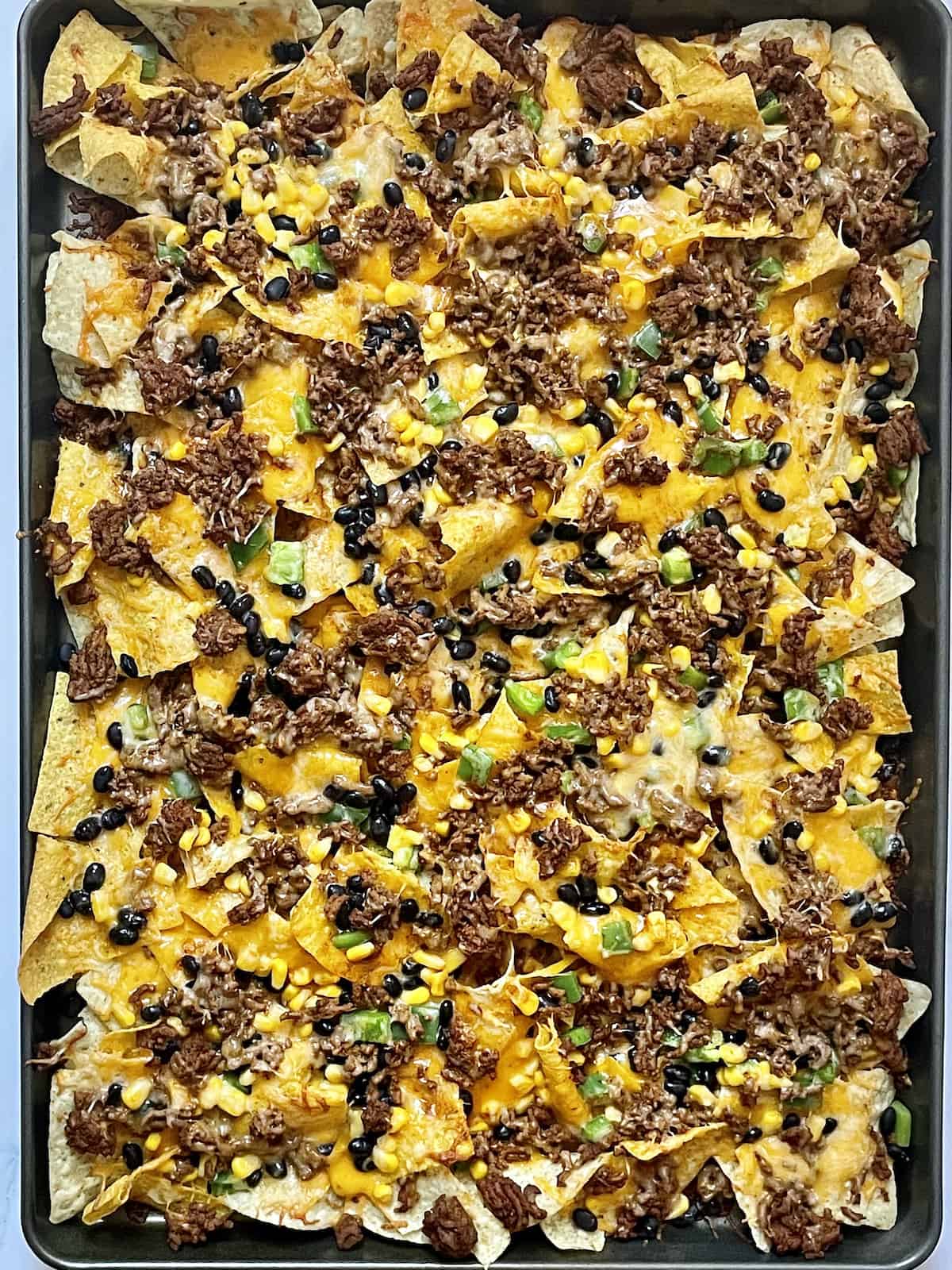 tortilla chips topped with cheese, beans, peppers, and beef cooked on a sheet pan