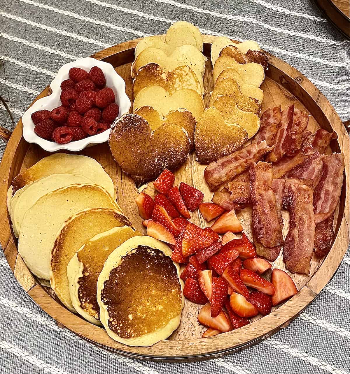 a breakfast pancake board with heart pancakes, bacon, strawberries, and raspberries