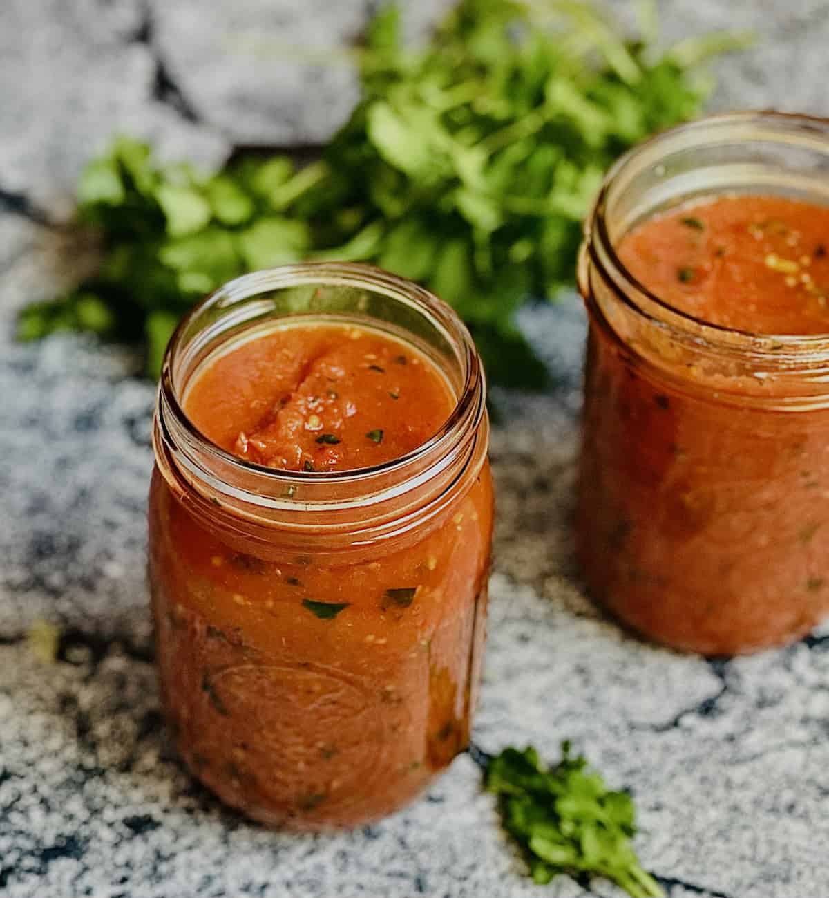 salsa roja in 2 mason jars surrounded by cilantro