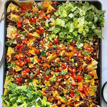 loaded sheet pan nachos with lettuce and veggies on a baking sheet