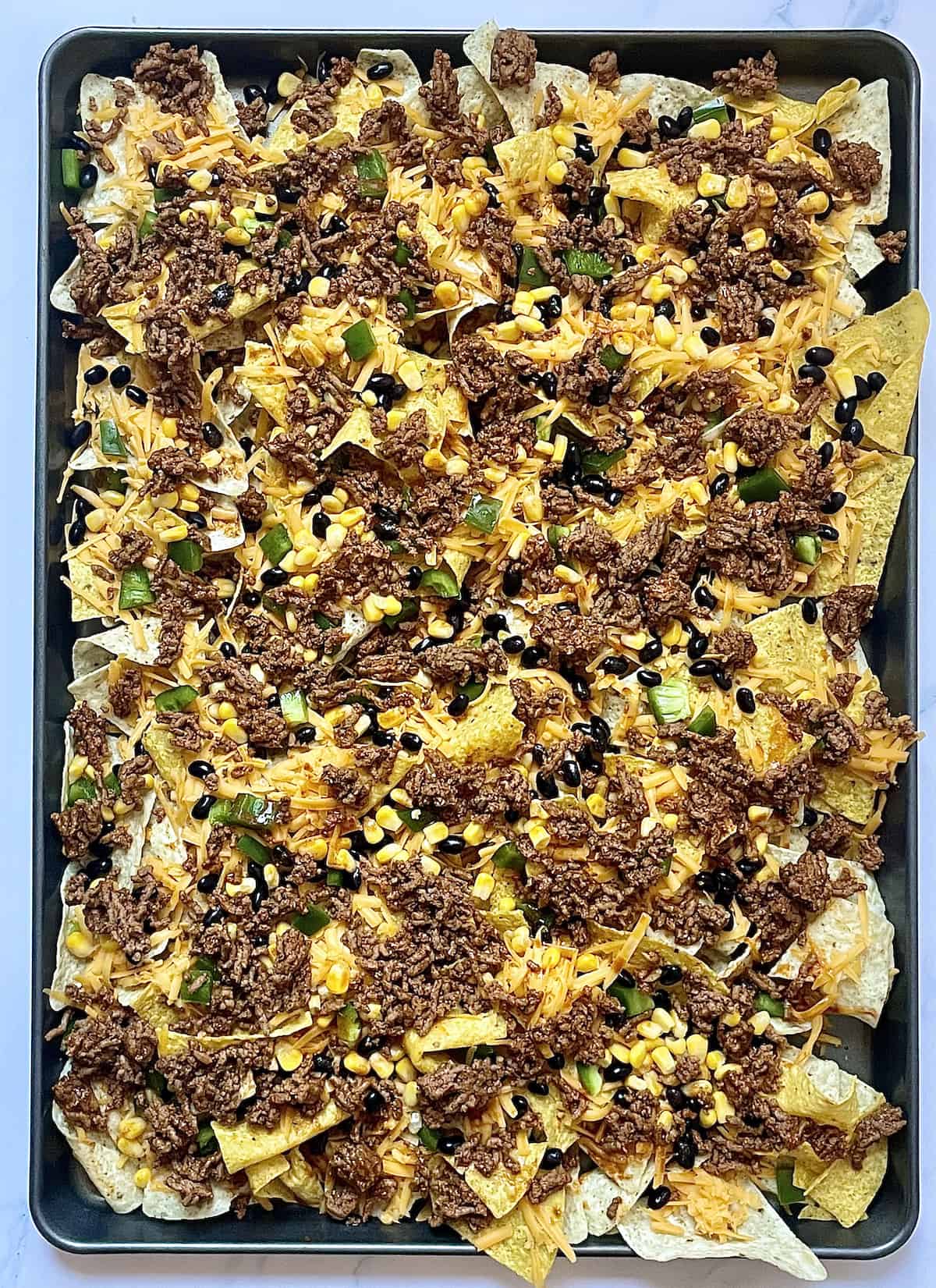 tortilla chips topped with cheese, beans, and peppers and ground beef on a sheet pan