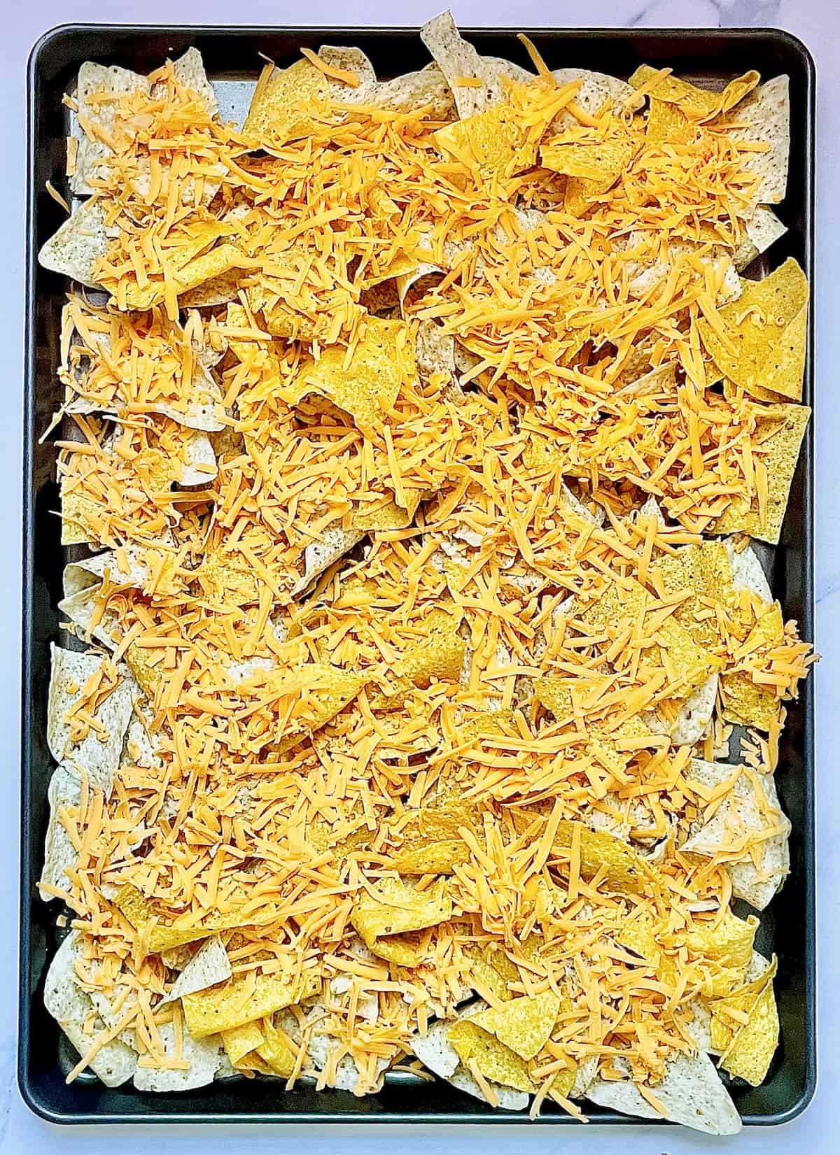 tortilla chips topped with cheese on a sheet pan