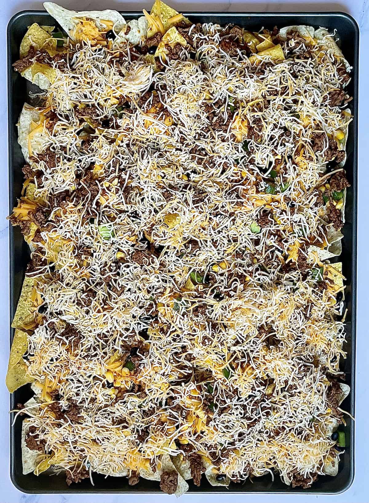 tortilla chips topped with cheese, beans, and peppers on a sheet pan