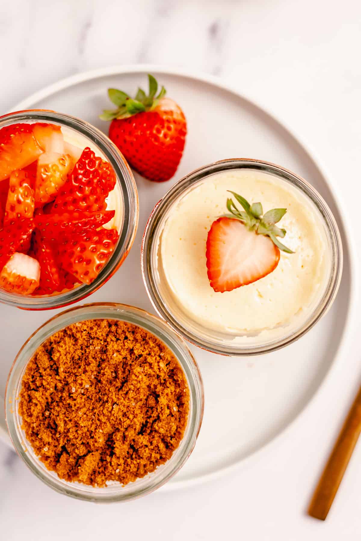 3 instant pot mini cheesecakes, one with crust on top, one with strawberries, and one with diced strawberries on a white plate 