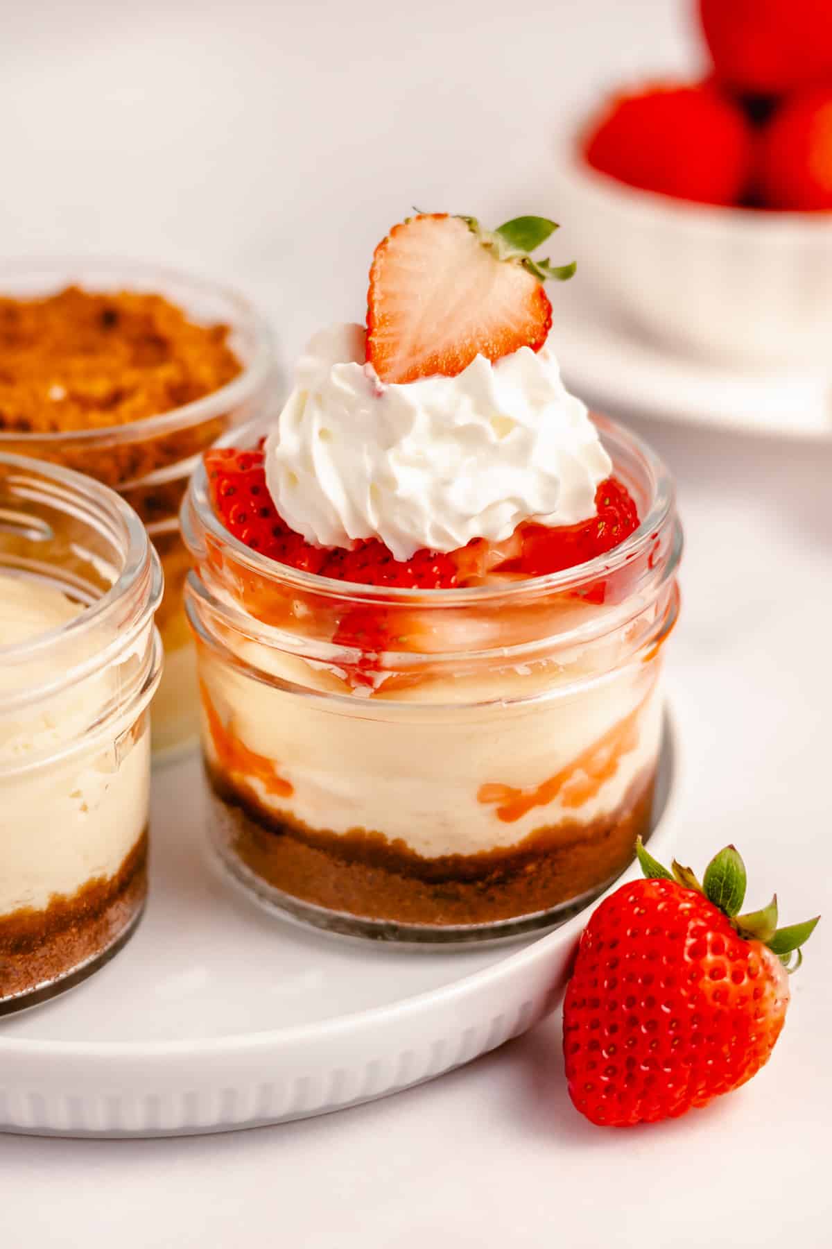 mini cheesecakes in small mason jars topped with strawberries and whipped cream