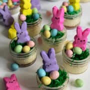 Mini Easter cheesecakes in jars decorated with coconut grass, chocolate eggs, and a bunny peep