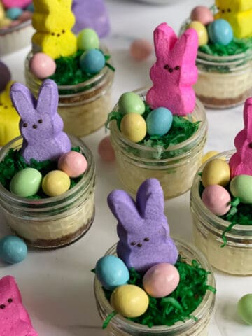 Mini Easter cheesecakes in jars decorated with coconut grass, chocolate eggs, and a bunny peep