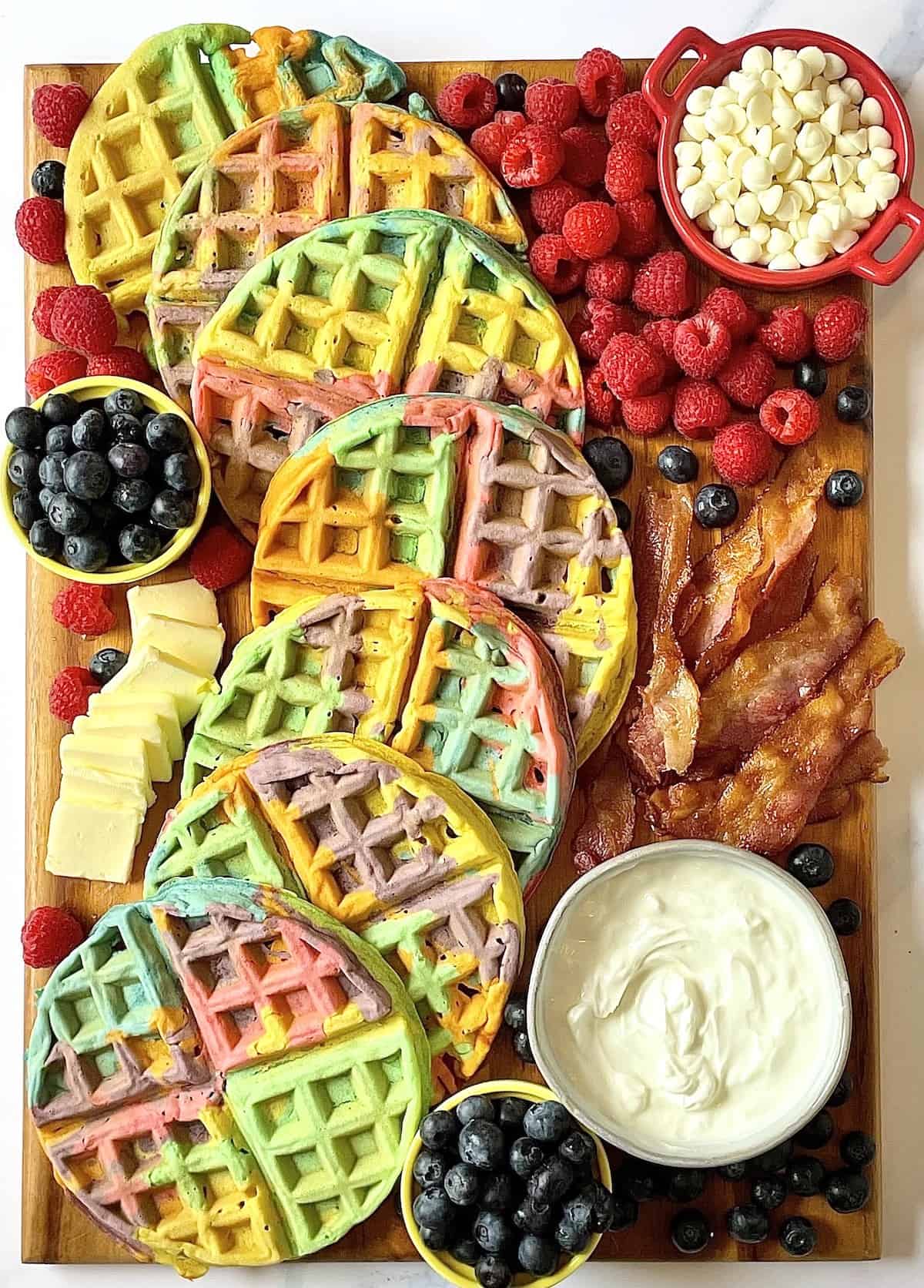 rainbow waffles, bacon, and fruit on a charcuterie board