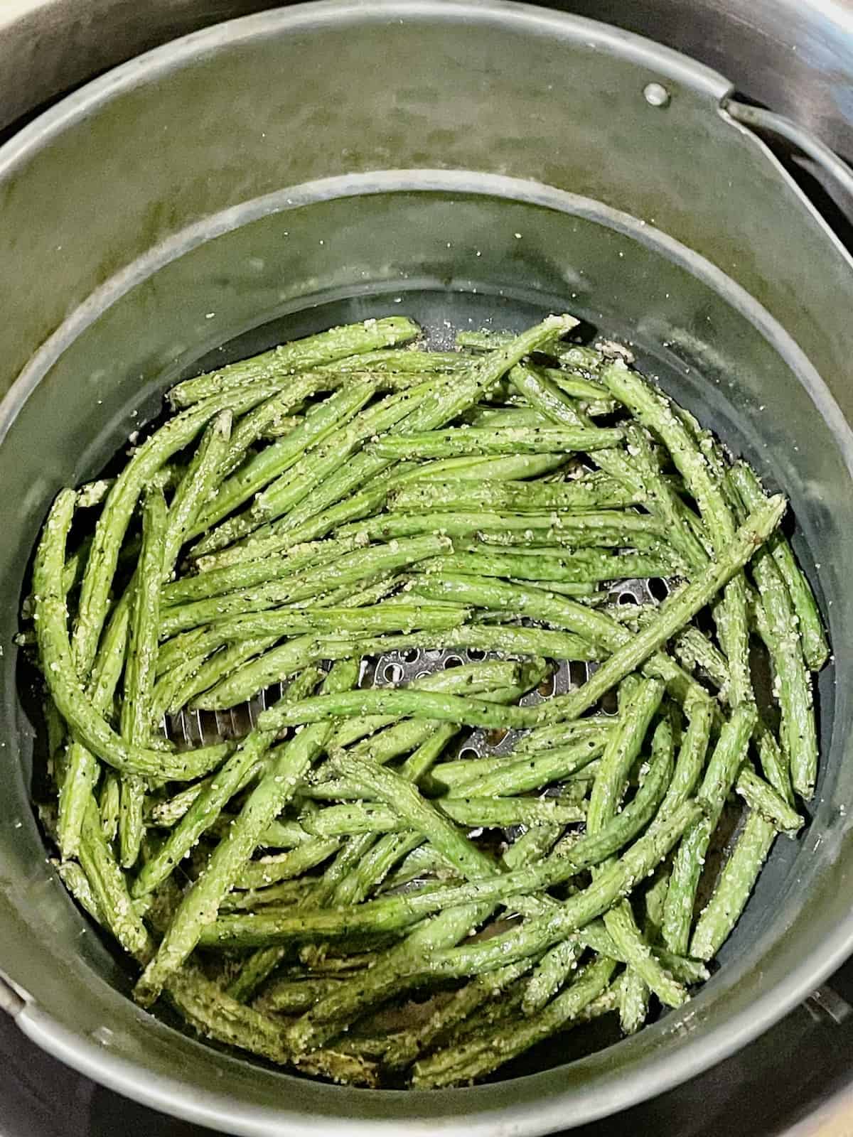 green beans in an air fryer basket tossed with salt and pepper