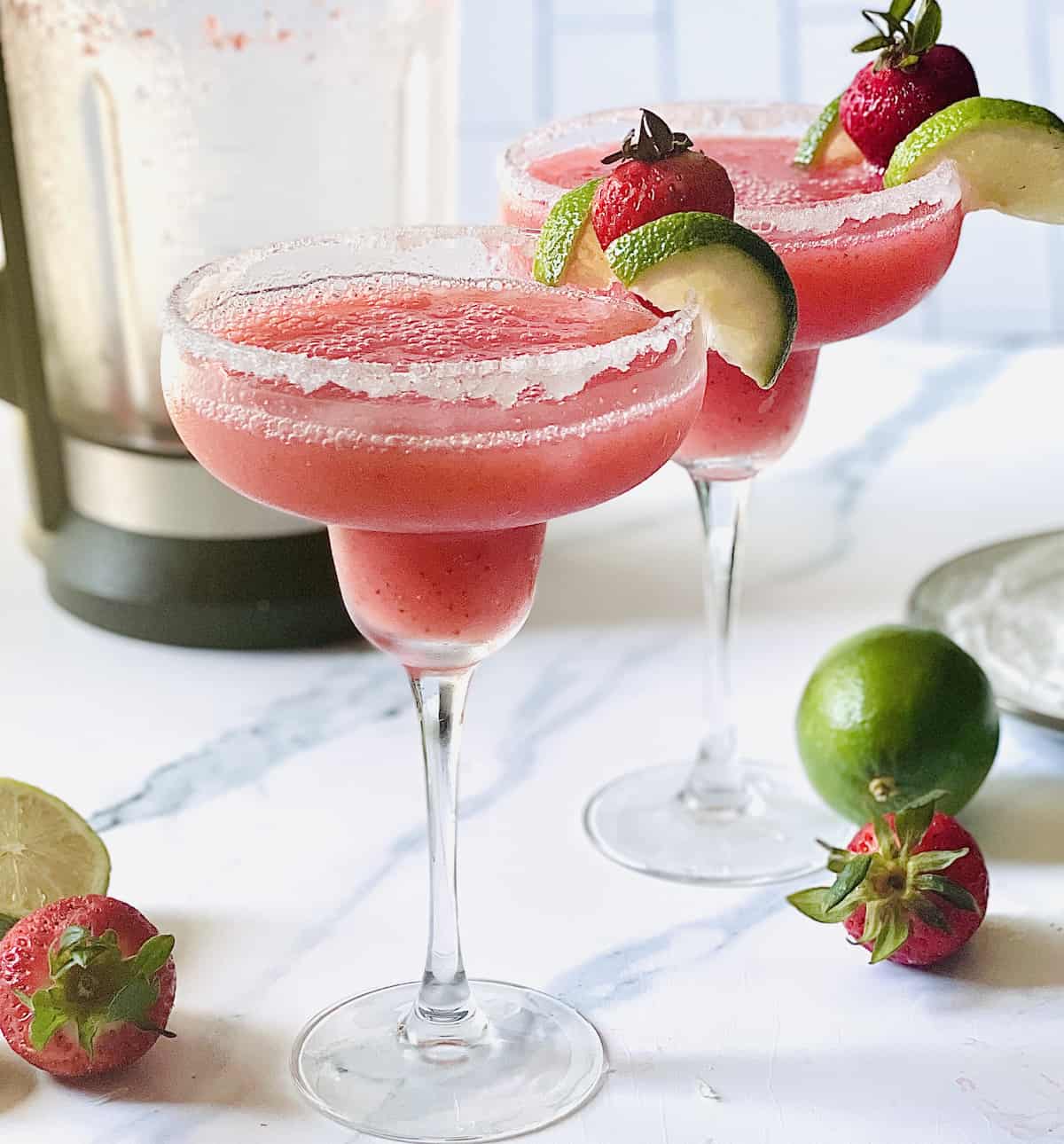 frozen strawberry margarita in a glass lined with sugar and in front of a cooking blender