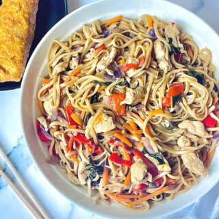 Instant Pot chicken lo mein in a white plate with an egg roll and chopsticks