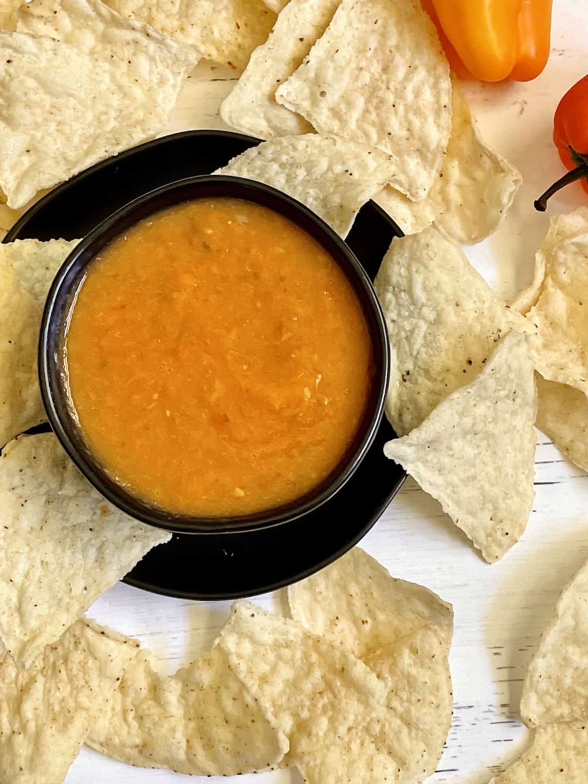 mango habanero salsa in a black bowl surrounded my tortilla chips