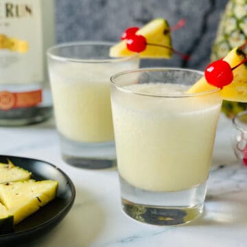 frozen pina colada in a small glass with cherries and pineapple garnish