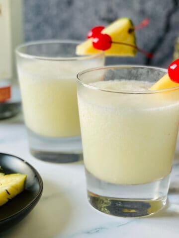 frozen pina colada in a small glass with cherries and pineapple garnish
