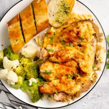 french onion chicken with vegetables and bread on a white plate
