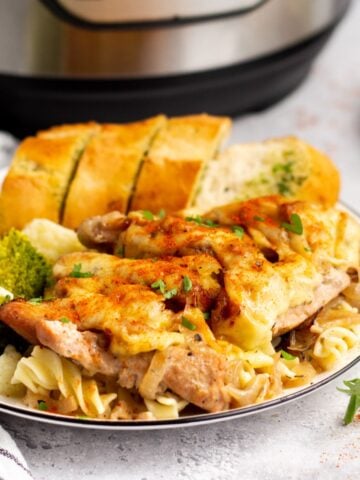 instant pot french onion chicken on a white plate with vegetables and garlic bread