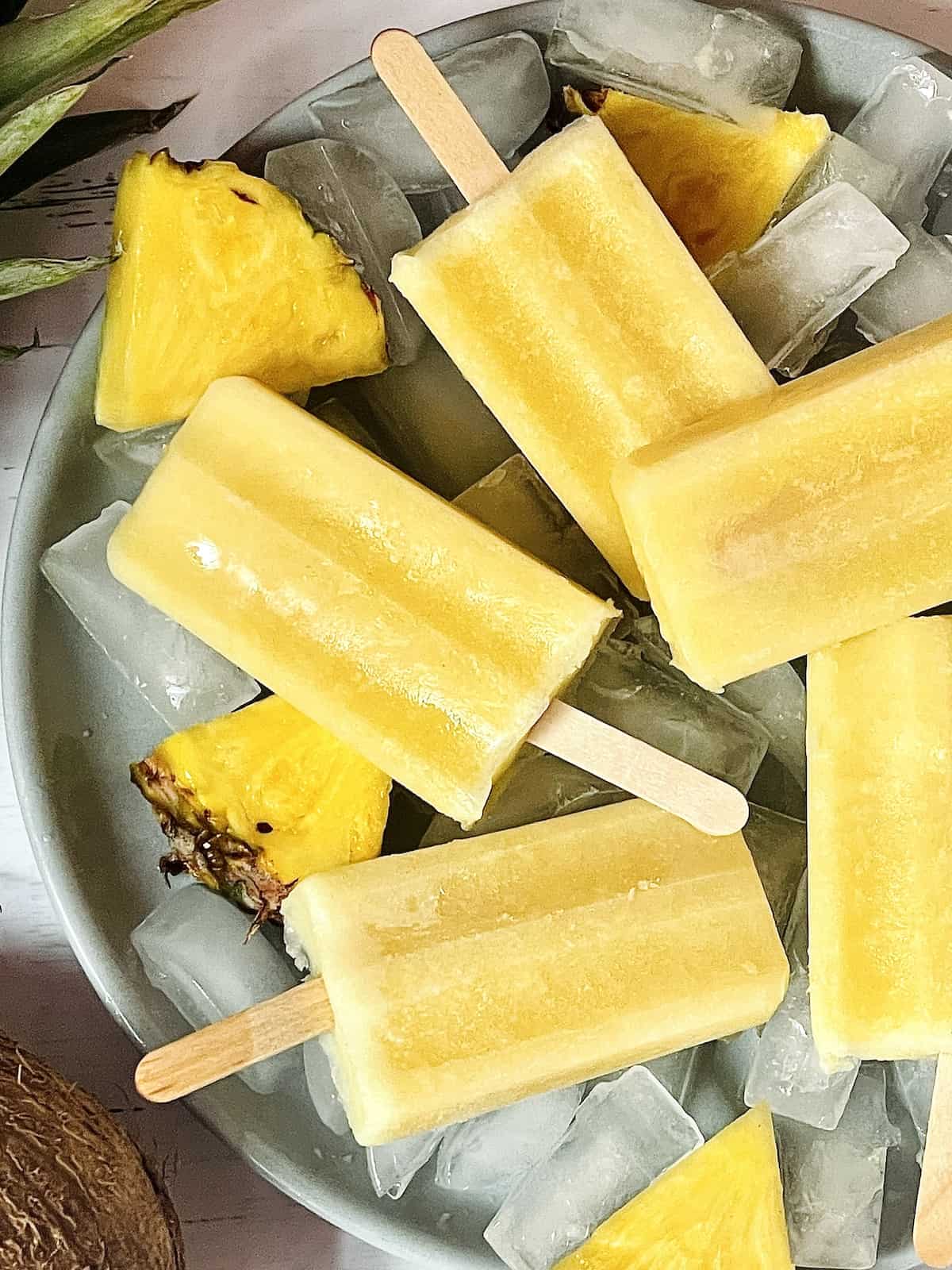 close up of yellow pineapple coconut popsicles on a grey plate over ice