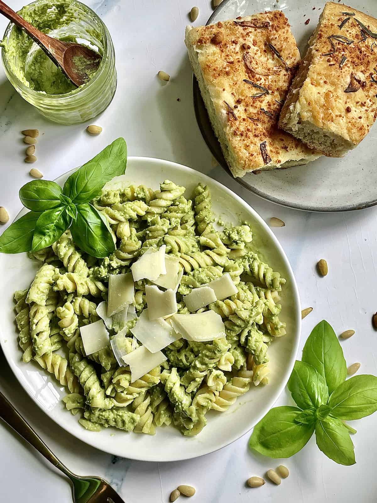 creamy pesto mixed with rigatoni pasta on a white plate topped with fresh basil leaves and parmesan cheese