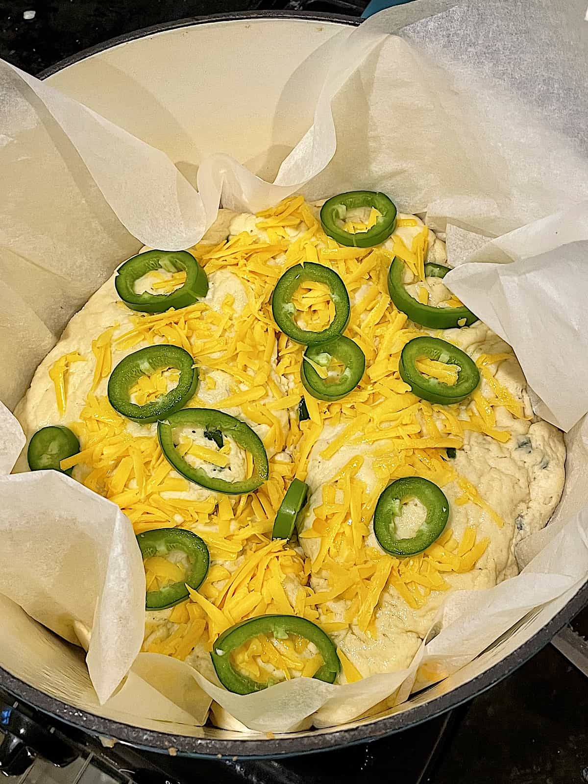 dough in a dutch oven topped with cheddar and jalapenos 