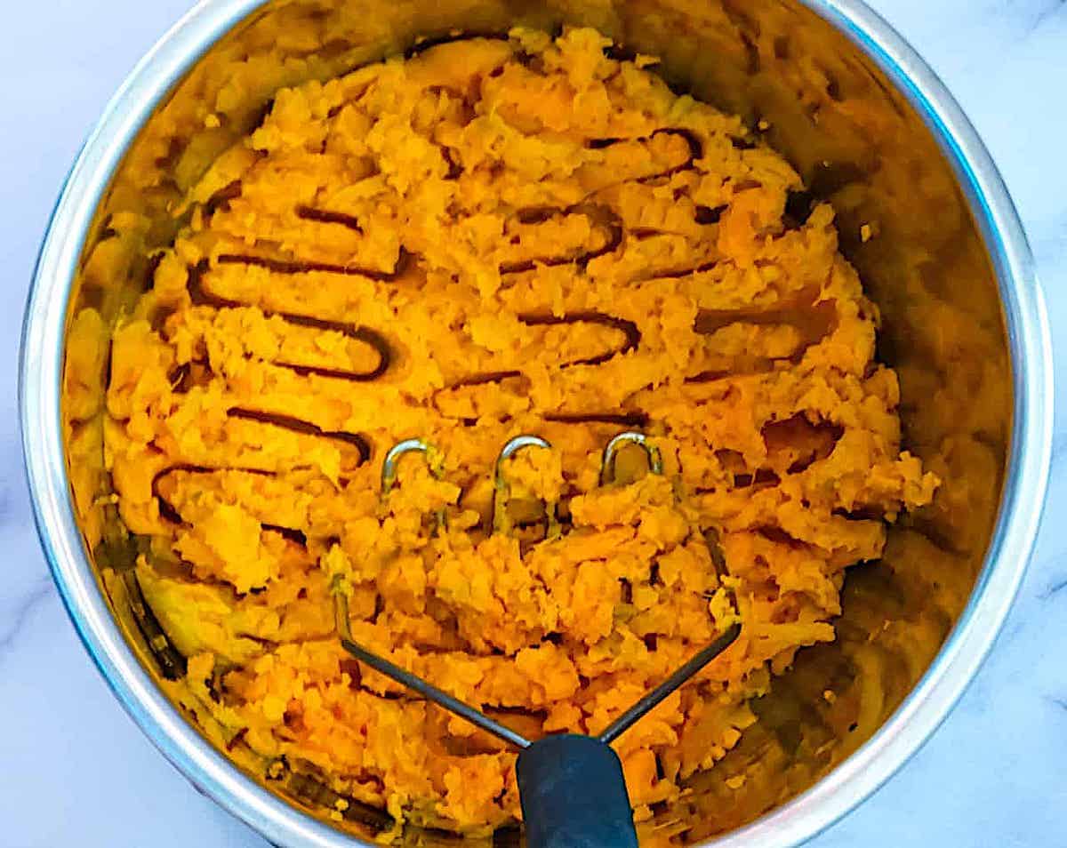 sweet potatoes being mashed with a potato masher in the Instant Pot