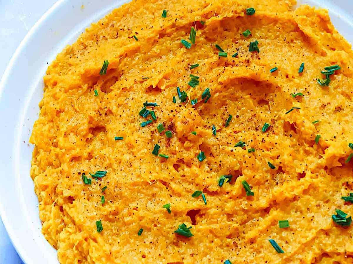 Mashed sweet potatoes mixed with herbs in a white serving bowl