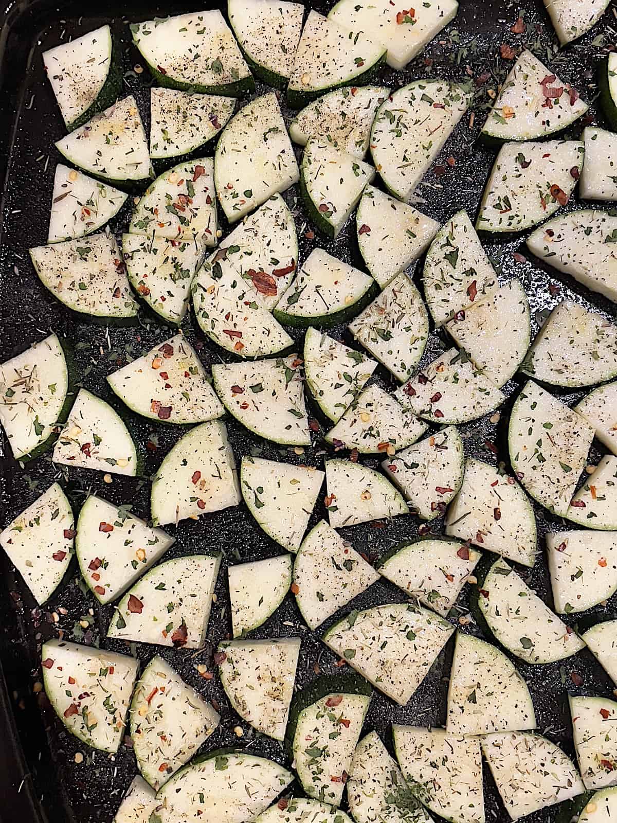 sliced zucchini sprinkled with salt, pepper, thyme, parsley, and red pepper on a baking sheet