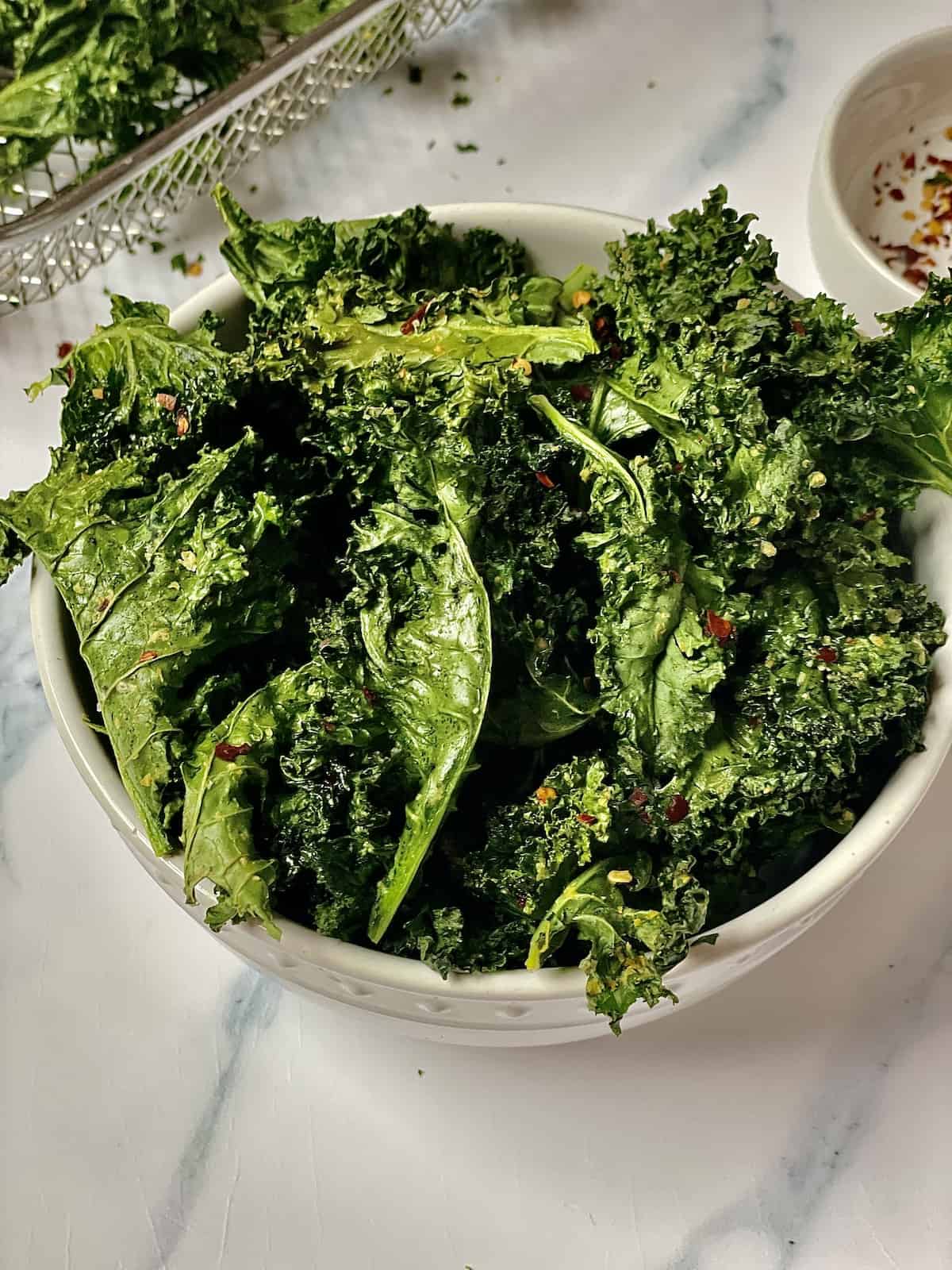 kale chips in a white bowl topped with red pepper flakes