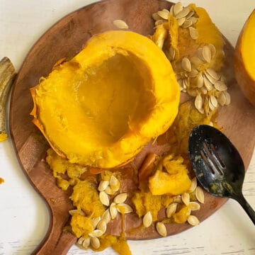 sliced whole pumpkin on a cutting board with seeds and pulp