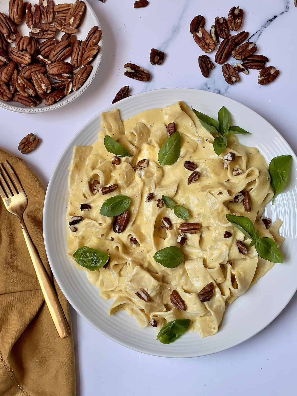 Instant Pot pumpkin pasta on a white plate tossed with pecan and fresh herbs