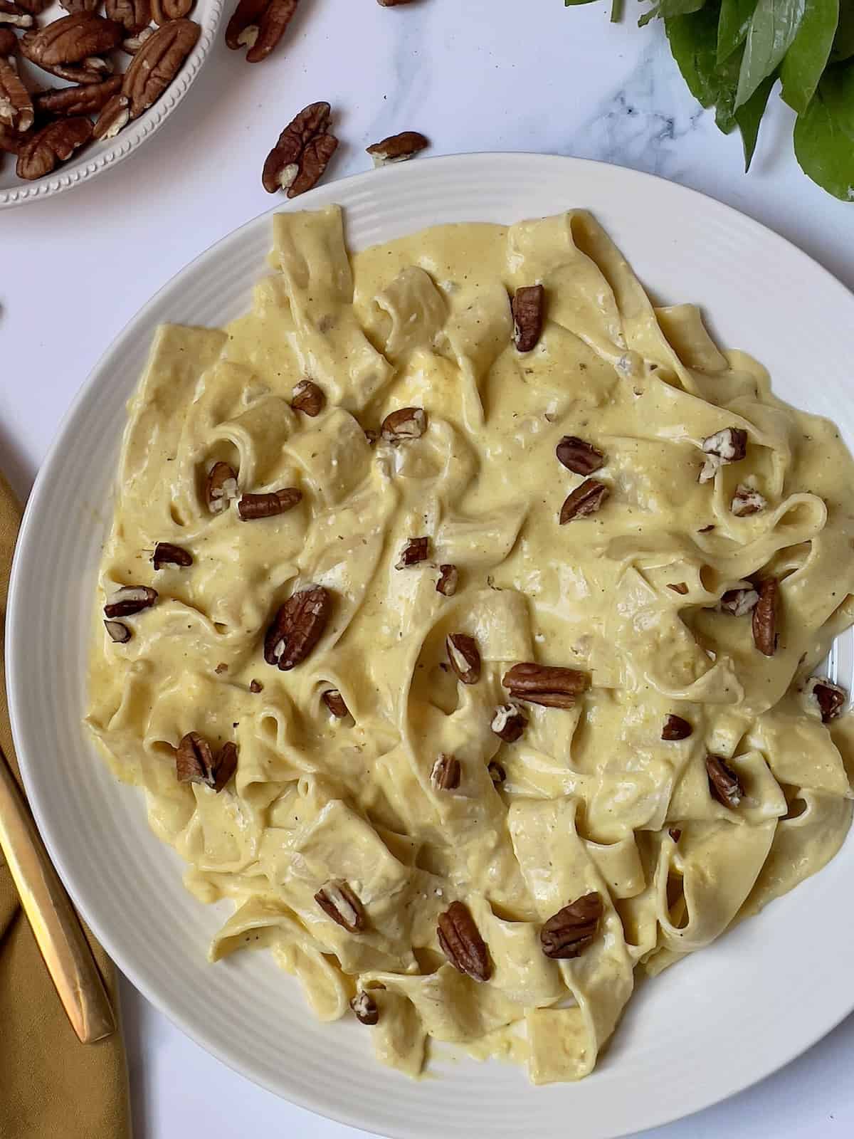 pumpkin pasta topped with pecans in a white bowl