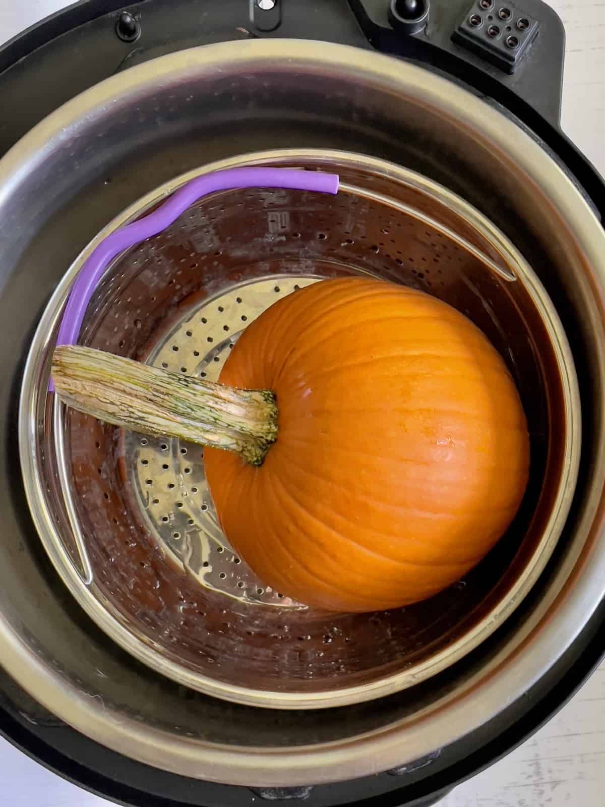 a whole pumpkin in a steamer basket of the instant pot