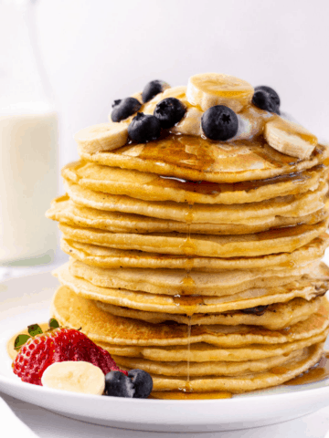 a stack of almond milk pancakes with blueberries, strawberries, and syrup