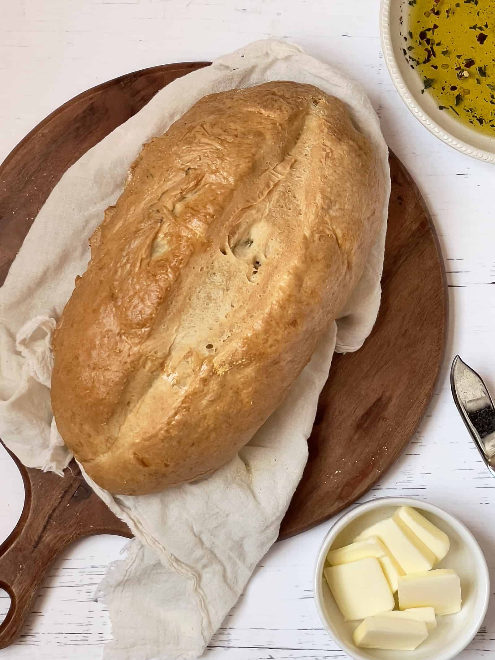 Italian bread loaf on a cutting board with dipping oil and butter