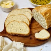 bread machine italian bread on a cutting board, sliced into pieces with butter and dipping oil